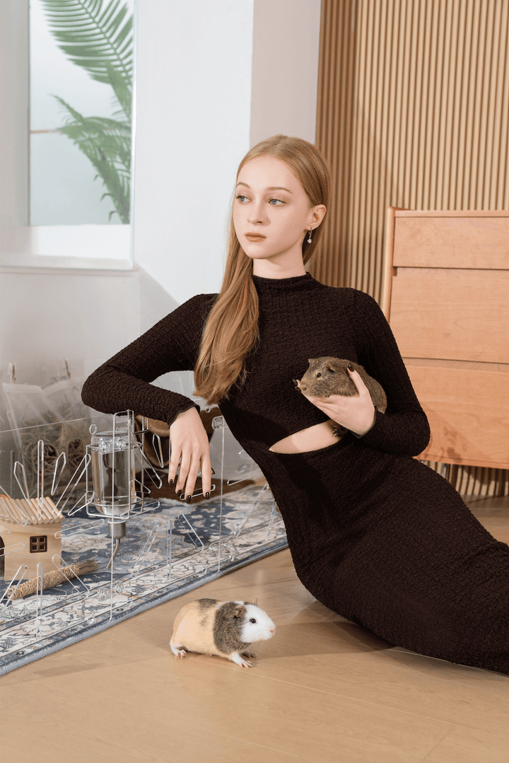 Guinea Colony Starter Kit - Critter Colony Club - Woman in a black dress holding a guinea pig leaning against an all clear guinea pig cage in a modern indoor setting